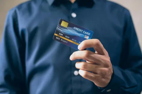 Close-up of a person holding a credit card in a hand, wearing a button-up shirt.