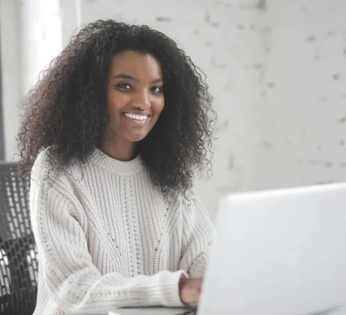 Smiling woman with curly hair using a laptop in a modern workspace, showcasing remote work confidence.