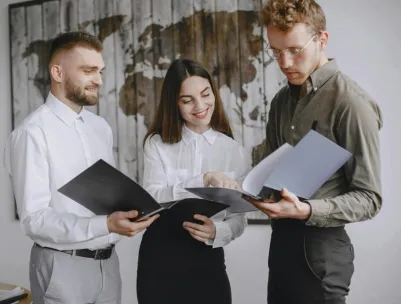 Three young professionals collaborating in an office, reviewing documents together with smiles and focus.