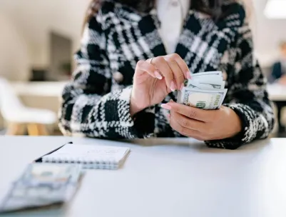 A close-up of a woman counting US dollars in an office environment, symbolizing financial management.