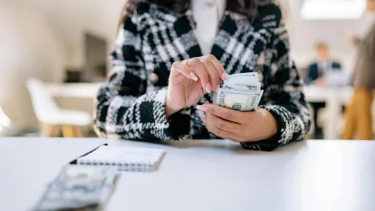 A close-up of a woman counting US dollars in an office environment, symbolizing financial management.