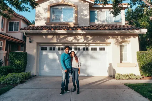 A joyous couple stands together in front of their newly purchased house, symbolizing new beginnings.