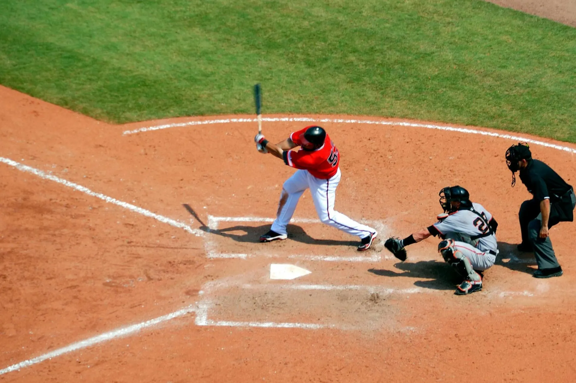 Action shot of a baseball game with batter swinging, catcher, and umpire observing play.