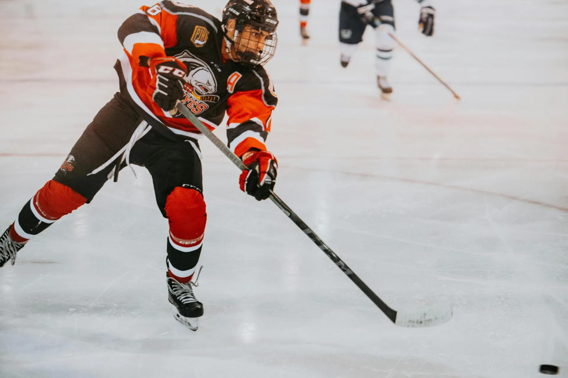 A male ice hockey player in full gear skates aggressively on ice during a game.