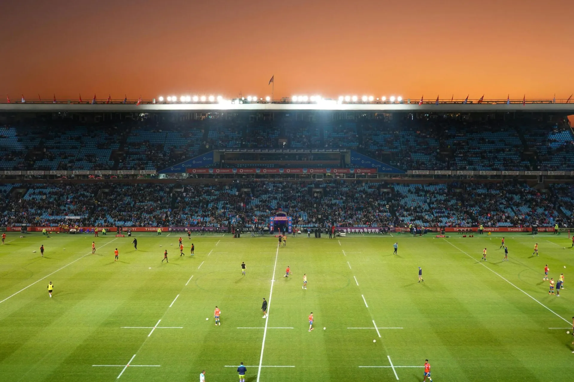 Exciting rugby game unfolding under stunning sunset in large stadium.