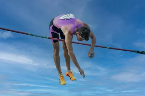 Dynamic capture of a pole vaulter clearing the bar under a clear blue sky.