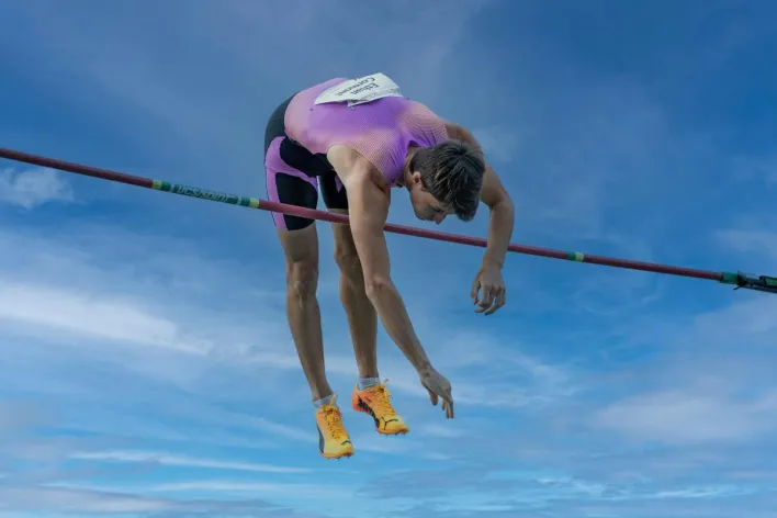 Dynamic capture of a pole vaulter clearing the bar under a clear blue sky.