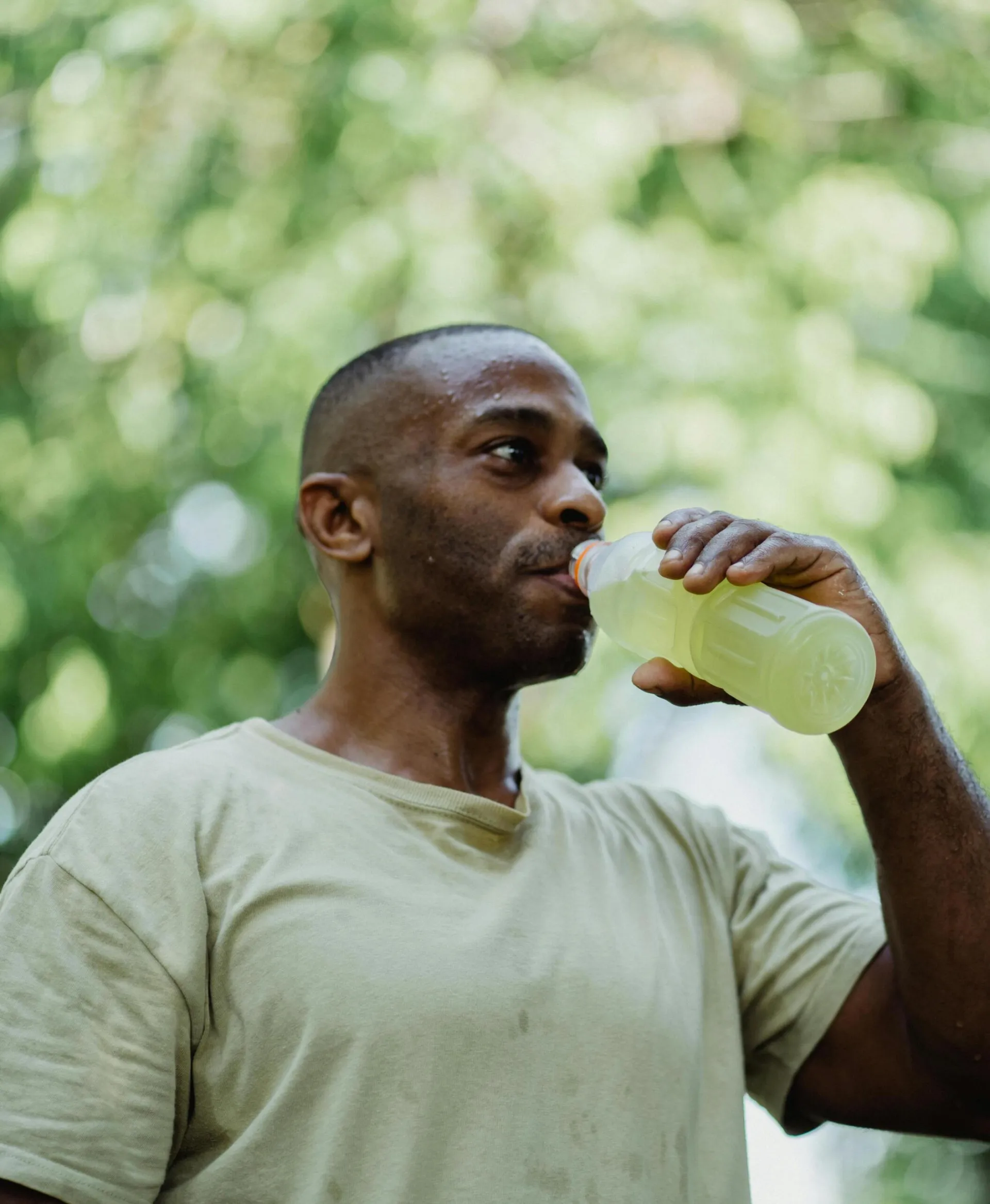 Athletic man drinking an energy drink outdoors in summer.