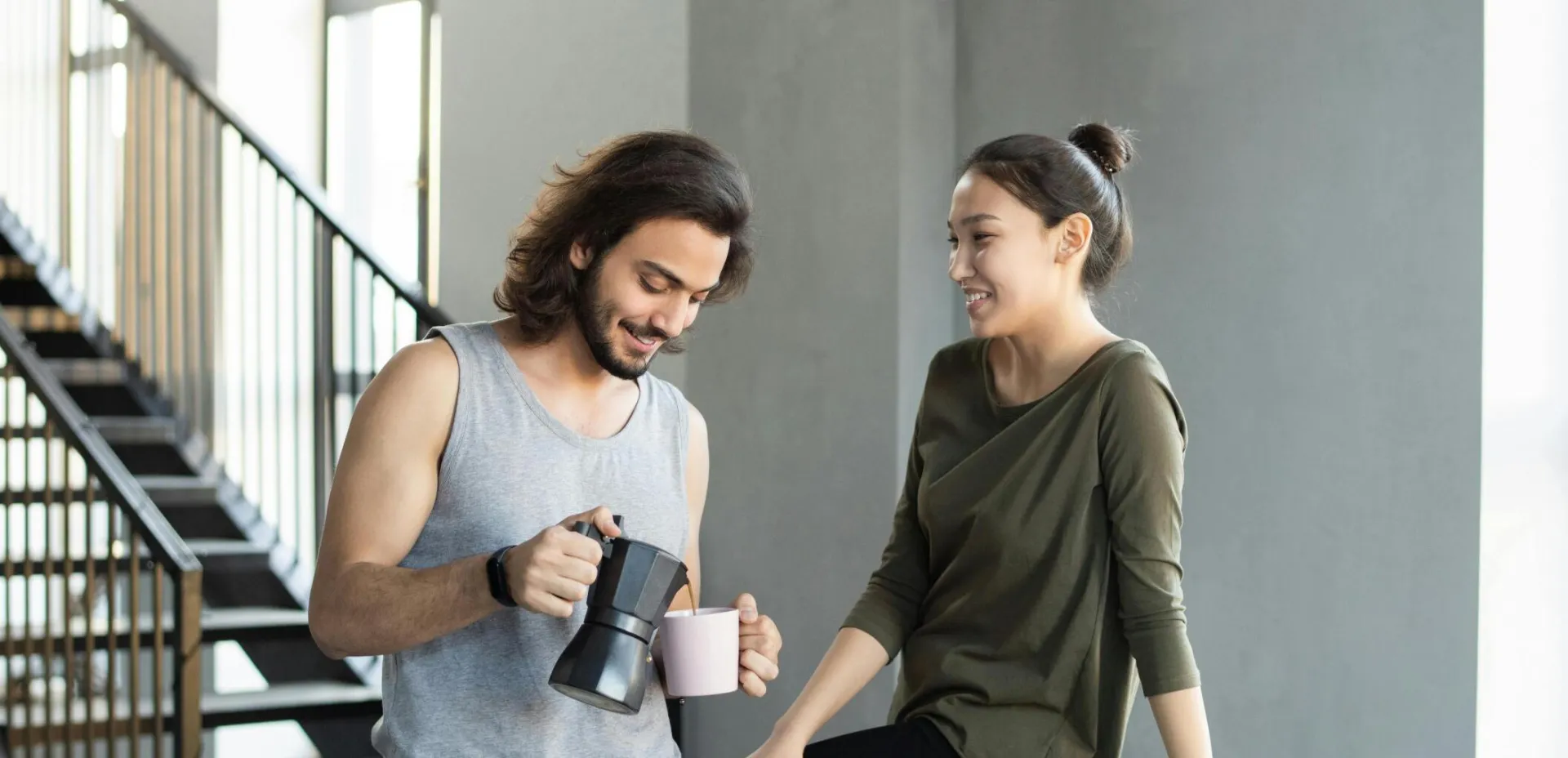 A couple enjoy a casual breakfast indoors with coffee and food, smiling and relaxed.