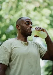 Athletic man drinking an energy drink outdoors in summer.