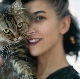 Close-up of a woman lovingly holding a fluffy tabby cat indoors.