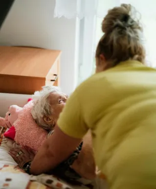 Nurse assisting elderly woman in a comfortable medical facility setting.