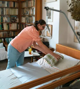 A caregiver adjusts bedding in a cozy home library setting in Prague.