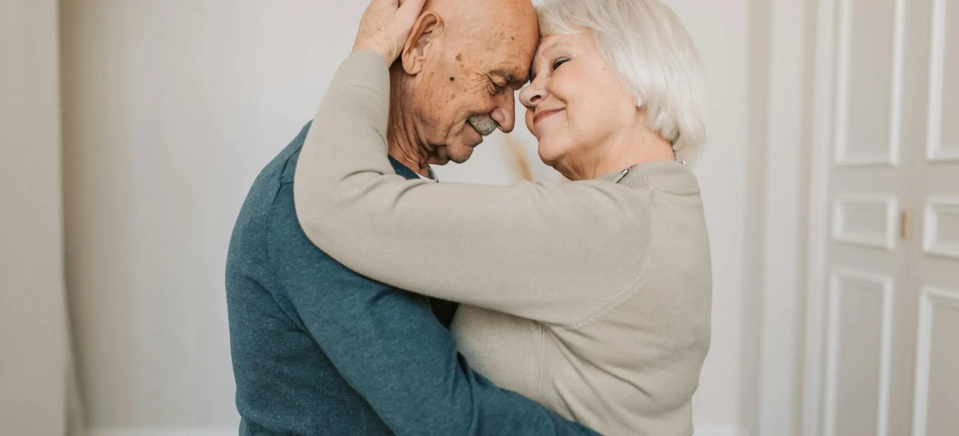 A joyful elderly couple embracing indoors, expressing love and happiness.