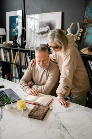 Elderly couple sharing a joyful moment together indoors with a notebook, books, and a cup of juice.