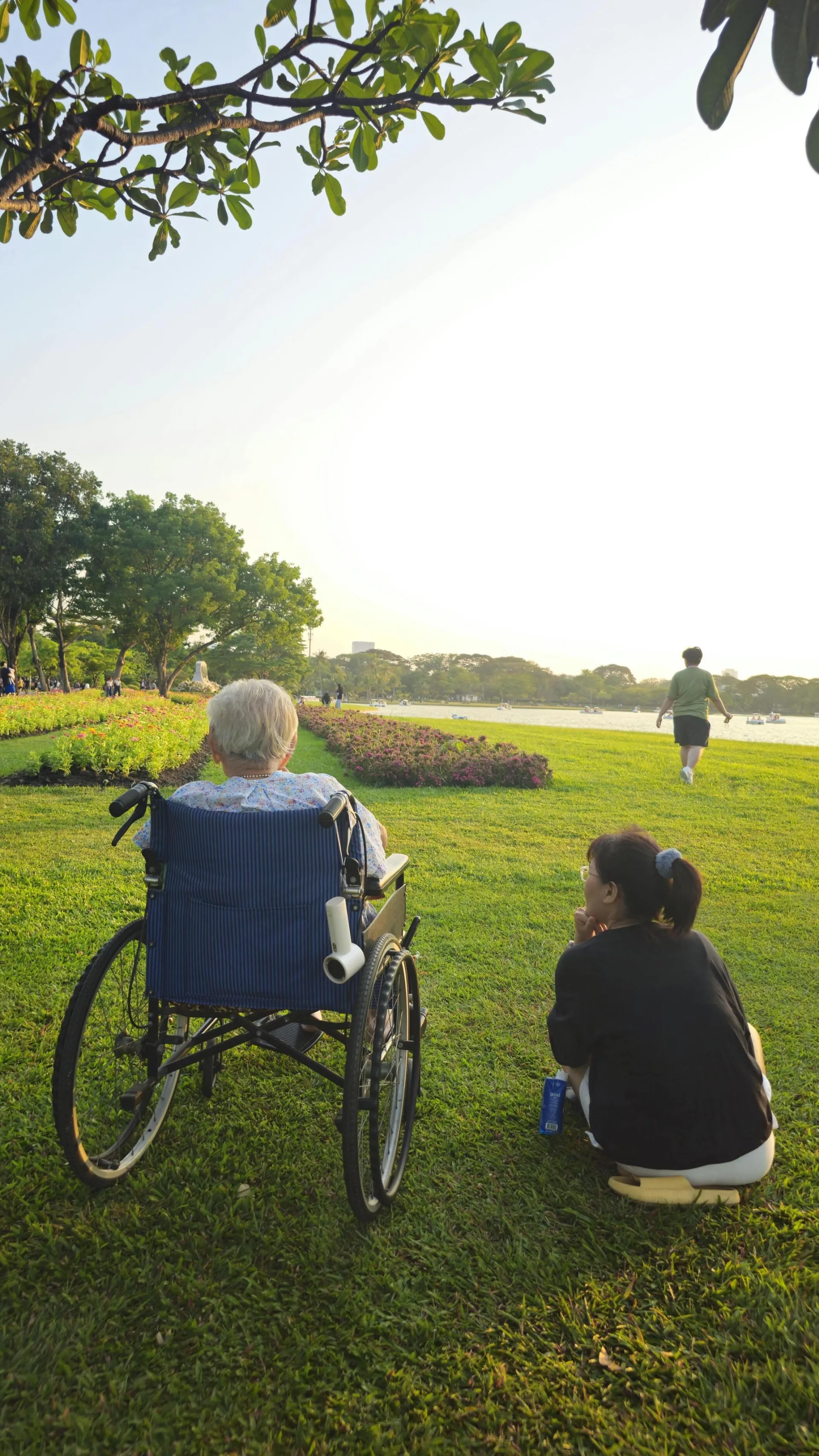 Elderly person and caregiver enjoy a serene afternoon by the river in Bangkok.