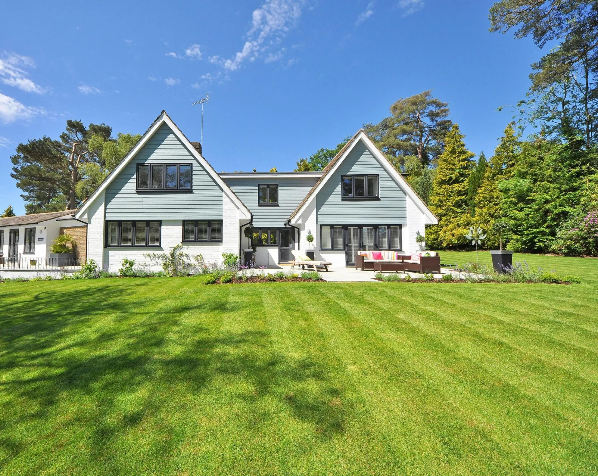 Modern family home exterior showcasing a large lawn and garden under a clear blue sky.