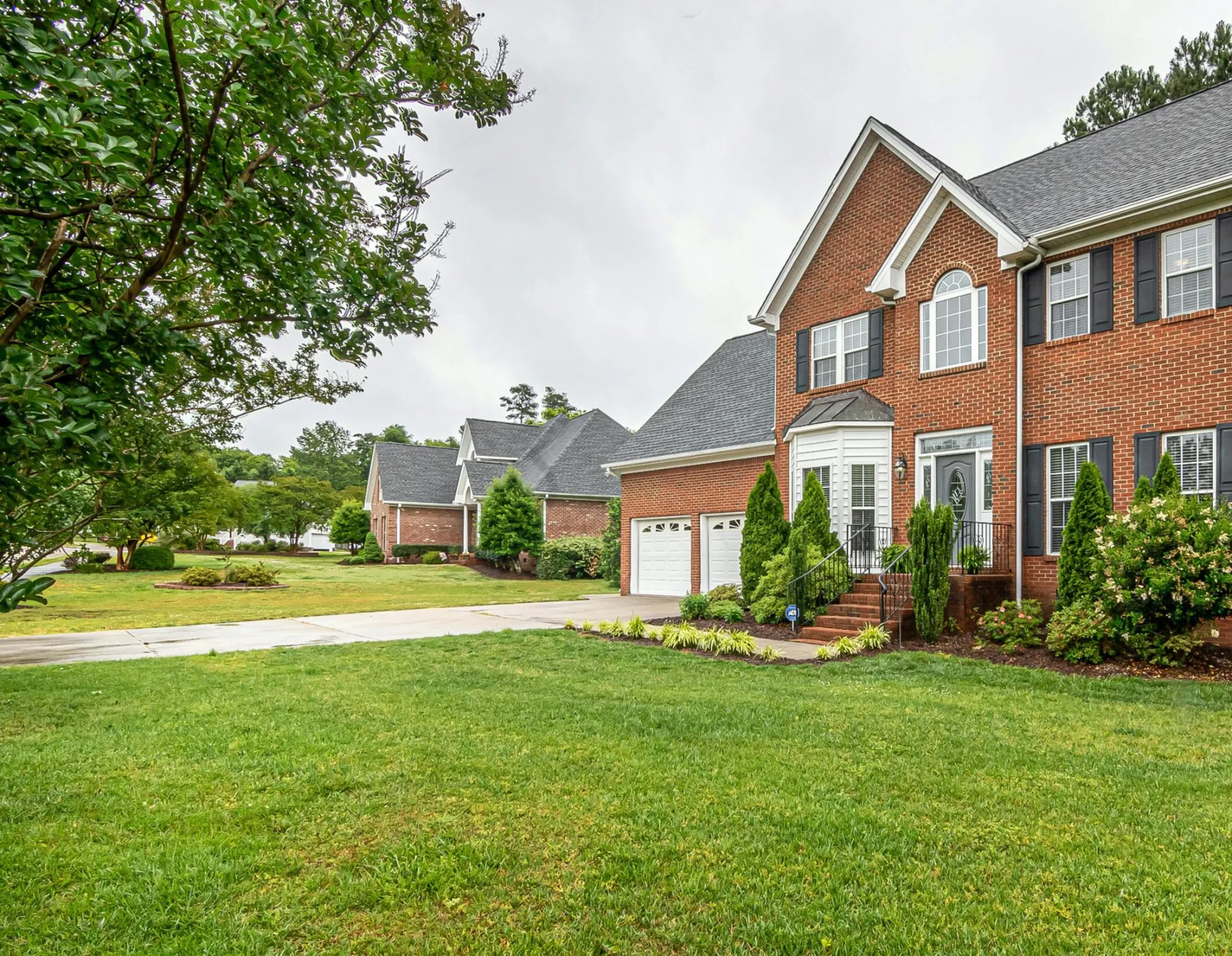 Charming two-story brick house with manicured lawn and trees, perfect family home.