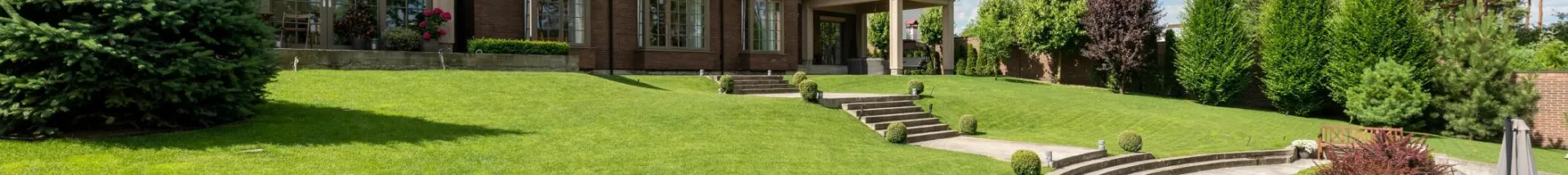 Elegant brick mansion with manicured lawn and garden under a bright blue sky.
