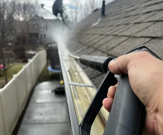 Close-up of gutter cleaning with pressure washer, outdoors, during the day.