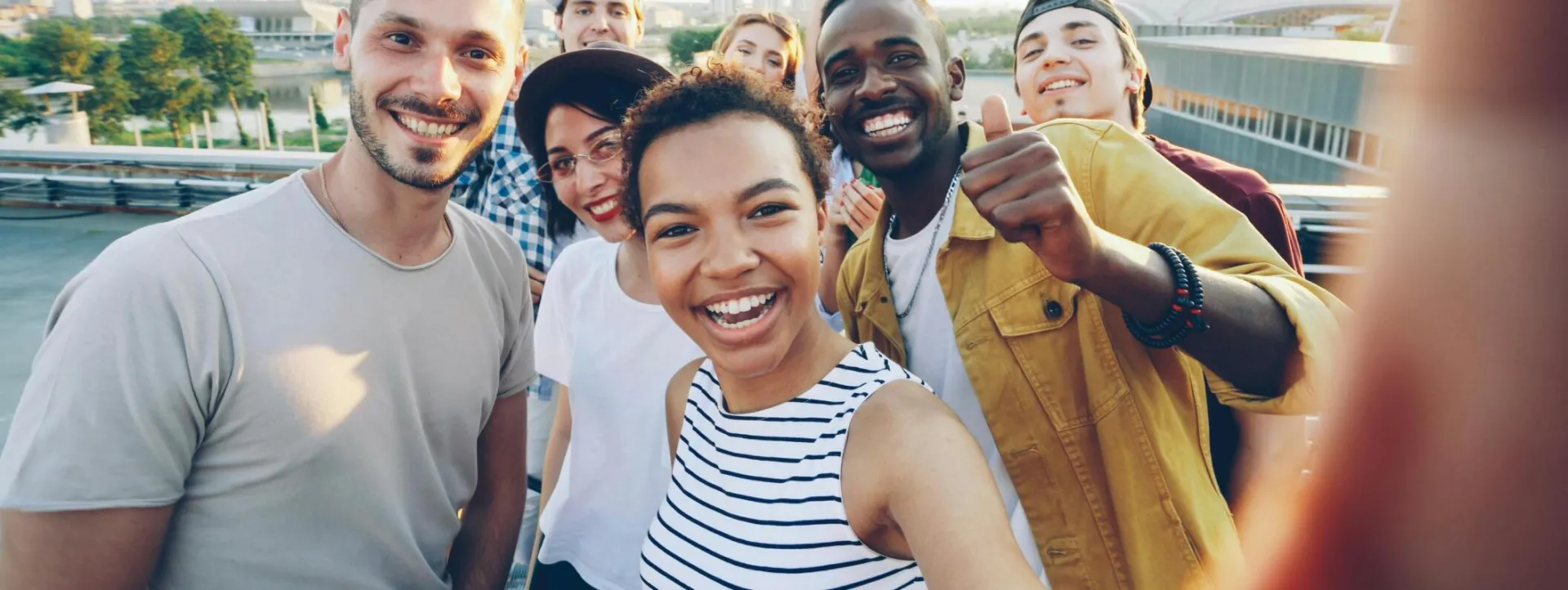 Diverse young friends smiling and posing for a rooftop selfie outdoors.