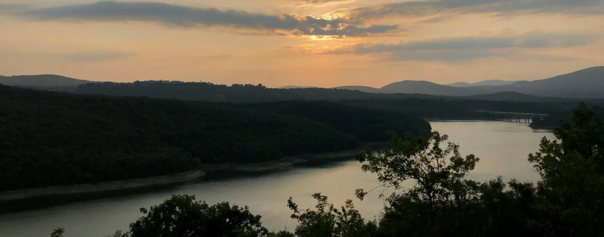 Beautiful sunset over a tranquil river surrounded by lush forests and hills.