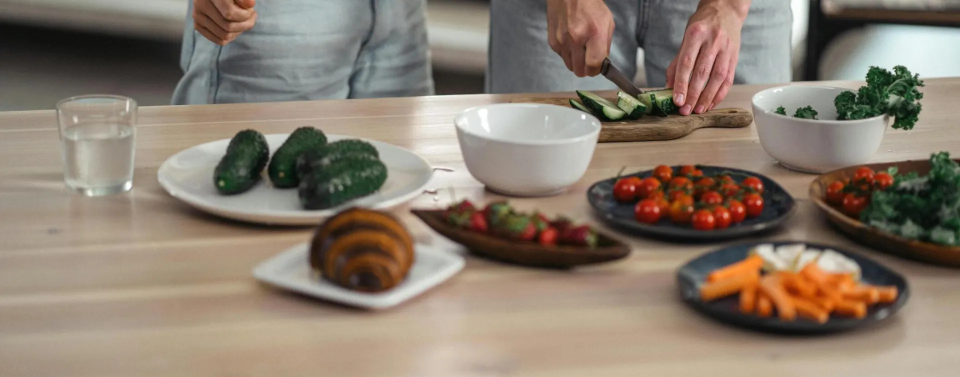 Two people preparing a healthy vegetarian meal with fresh vegetables and snacks on a wooden table.