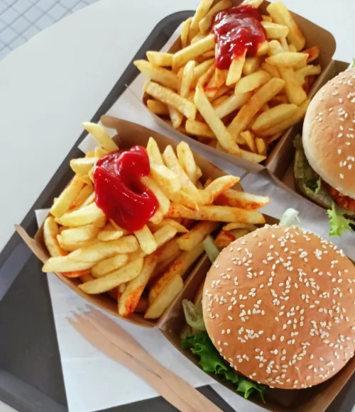 Top view of juicy burgers and crispy fries with ketchup served on a tray.
