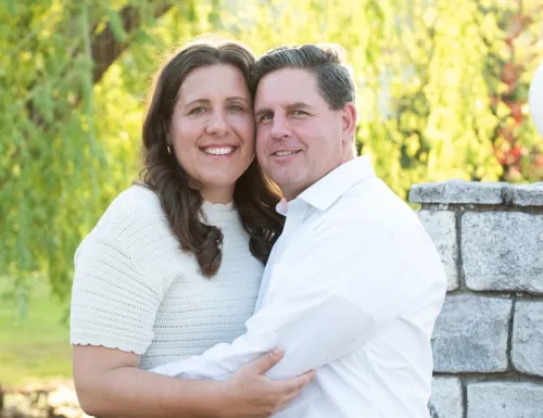 Happy couple smiling and embracing outdoors in a sunlit park, capturing a moment of joy and affection.