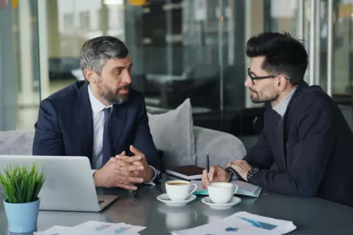 Two businessmen having a meeting with laptops, papers, and coffee at a modern office.