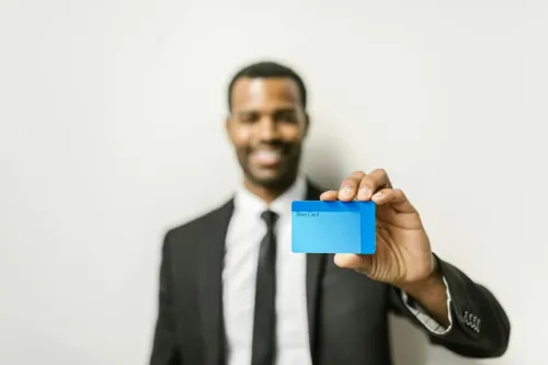 Smiling businessman in a suit presenting a blue credit card against a neutral background.