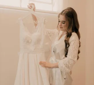 A bride admires her elegant white wedding gown, capturing a serene pre-wedding moment indoors.