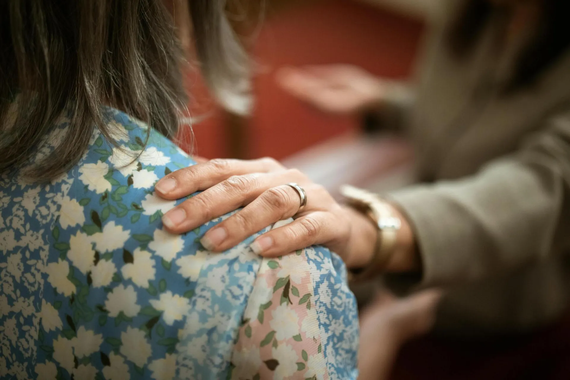 A supportive hand rests on a woman's shoulder, symbolizing empathy and care.