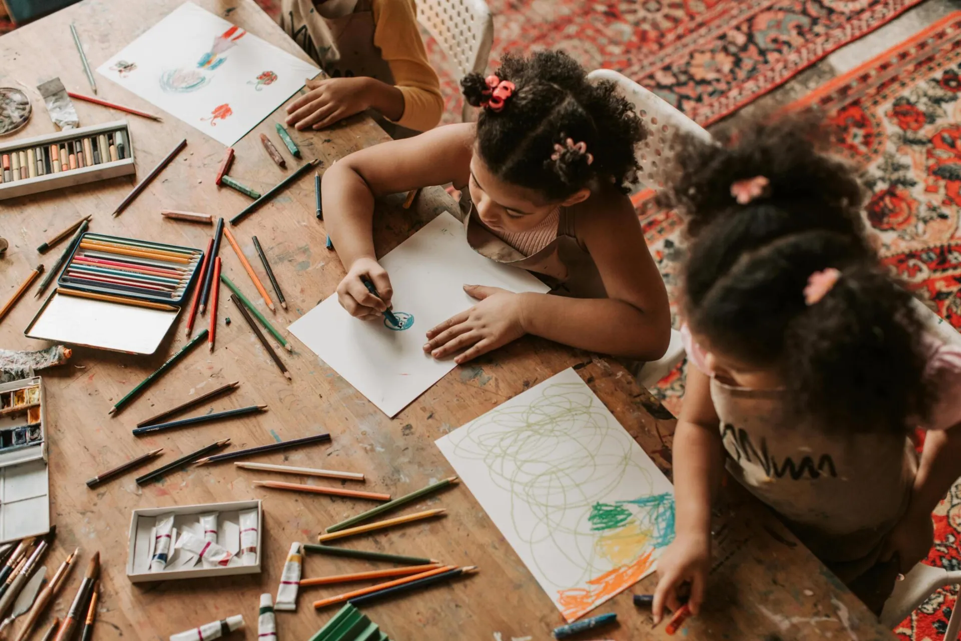 Children drawing with colored pencils and papers indoors, showcasing creativity.