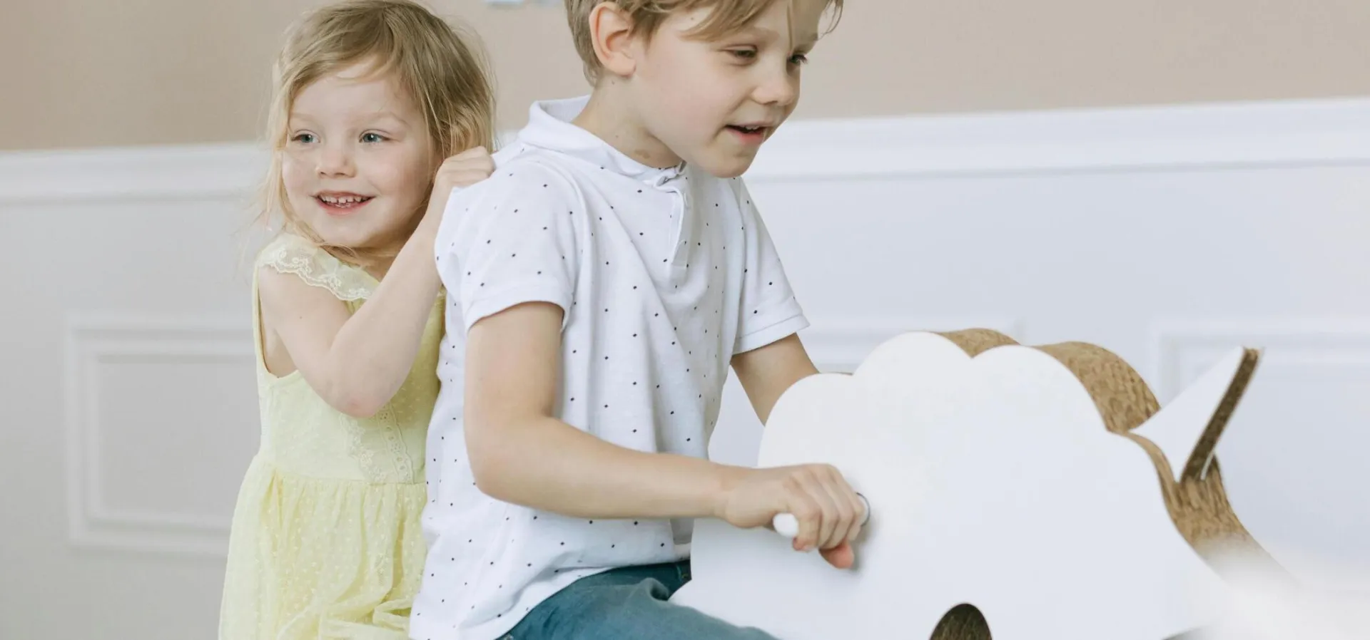 Two children having fun on a wooden rocking horse at a birthday celebration indoors.
