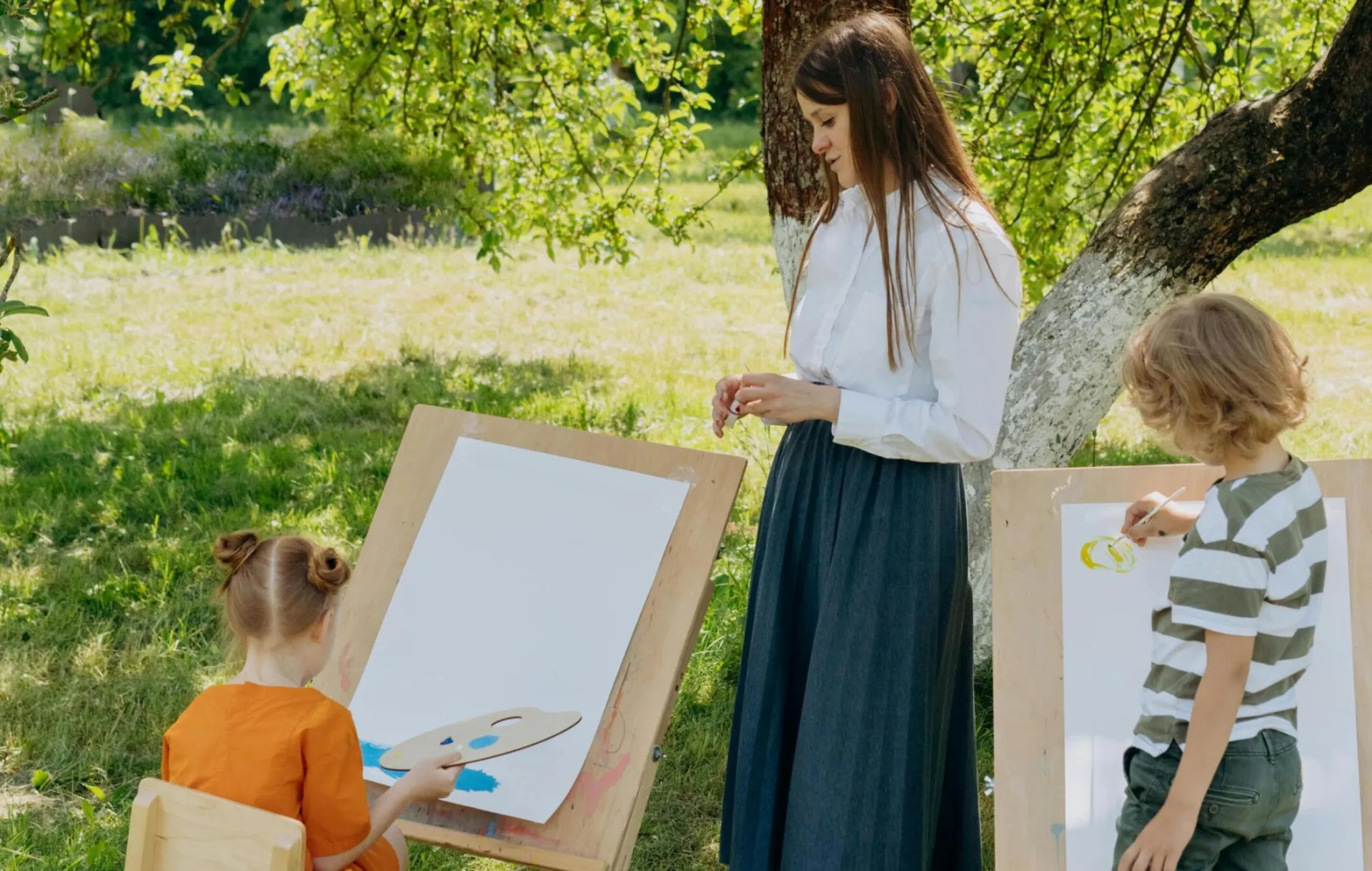 Children painting outdoors with a teacher, promoting creativity in nature.