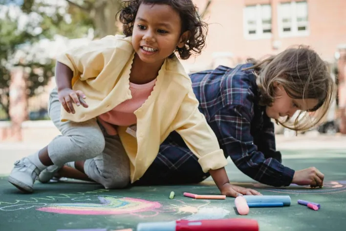 Children enjoying outdoor artwork with colored chalk on a sunny day.