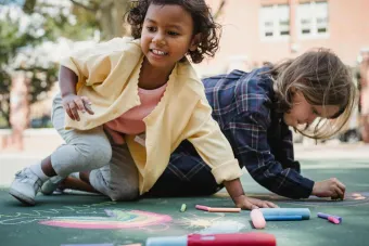 Children enjoying outdoor artwork with colored chalk on a sunny day.