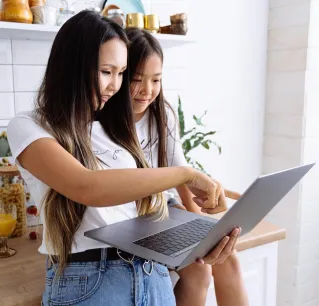 A mother and her daughter using a laptop together in a cheerful kitchen setting, bonding over technology.