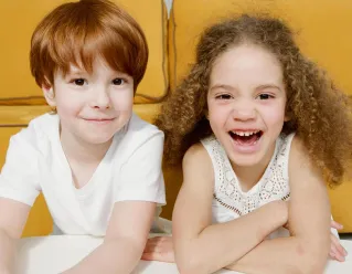 Two cheerful children smiling indoors, showcasing happiness and sibling bonding in a warm setting.