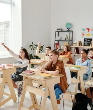 Students engage eagerly in a classroom, raising hands and participating in a lesson with their teacher.