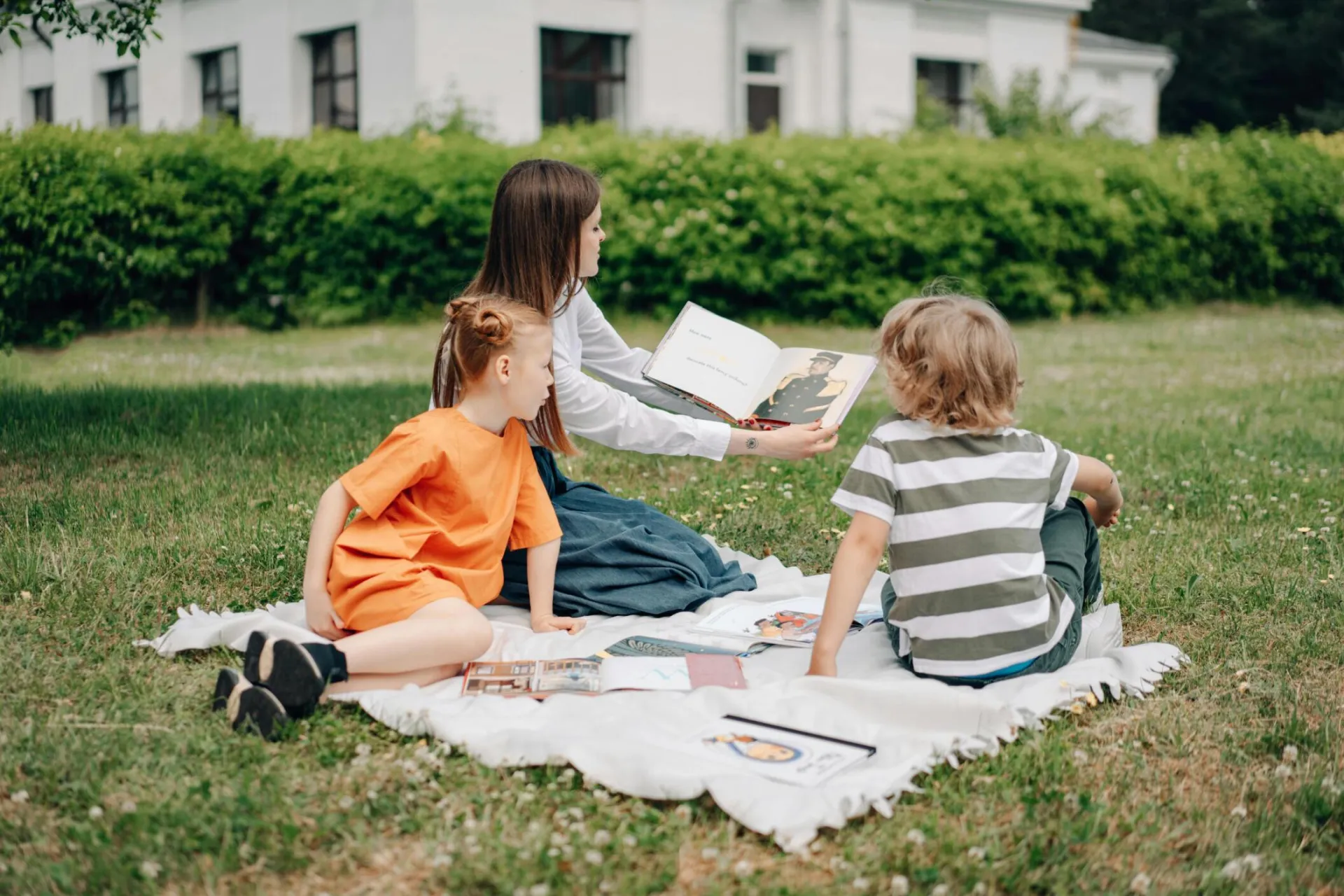 A woman teaching two children outdoors on a blanket, fostering education in nature.