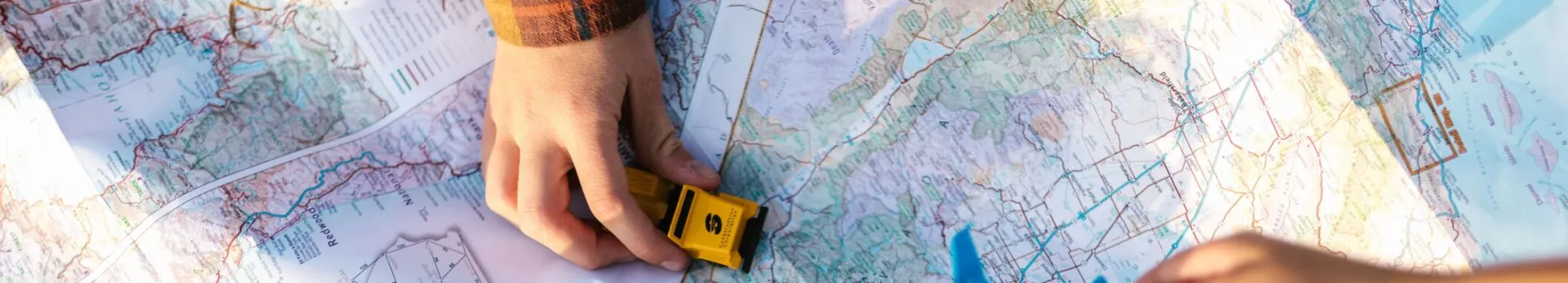 Hands holding a toy airplane and car over a map, symbolizing travel planning and exploration.