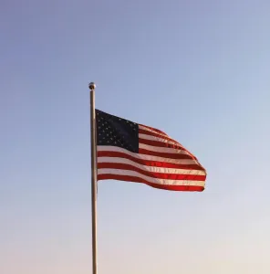 A United States flag waving on a flagpole against a clear blue sky, symbolizing patriotism.