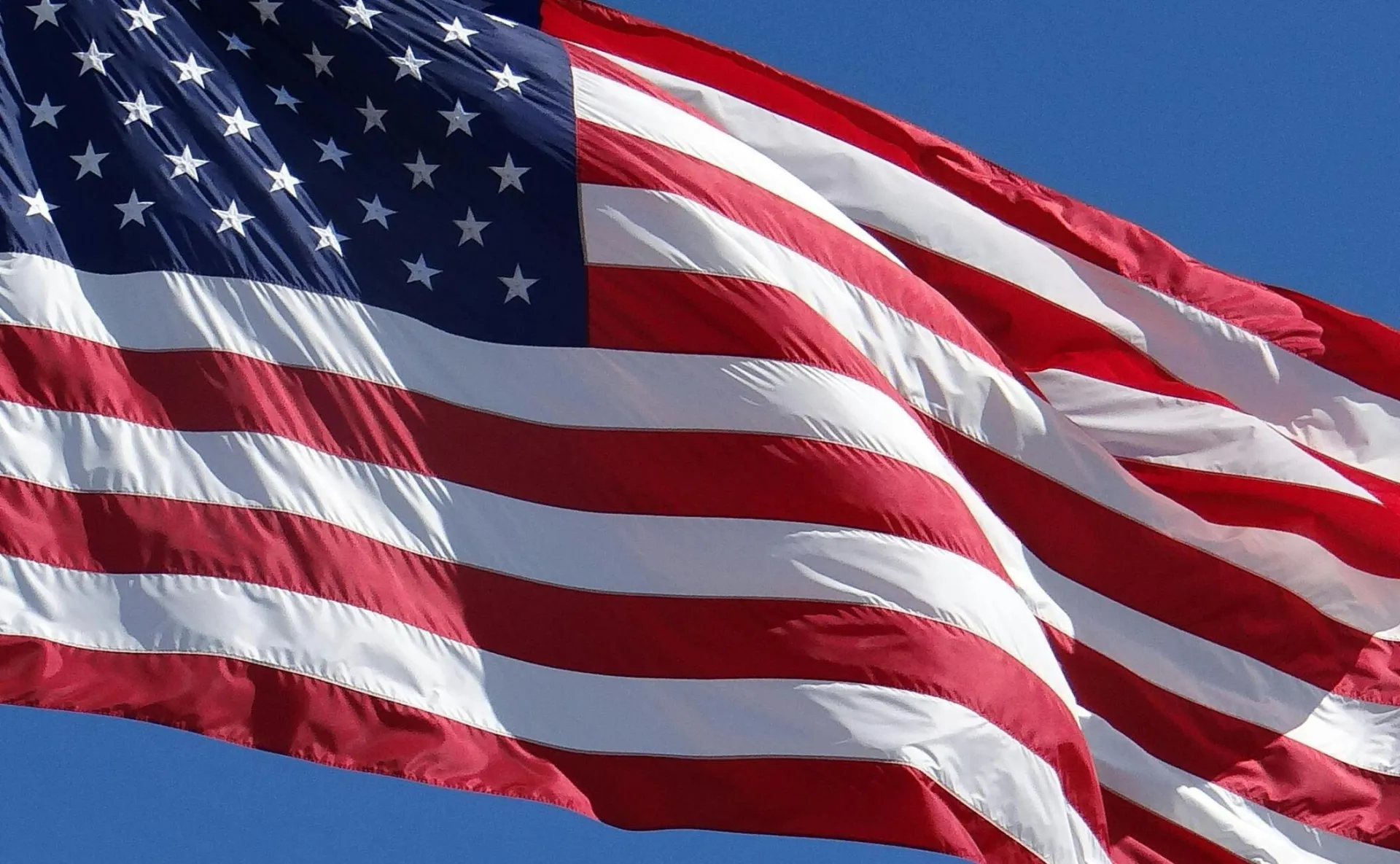 A vibrant American flag waves majestically against a clear blue sky in Mackinaw City, Michigan.
