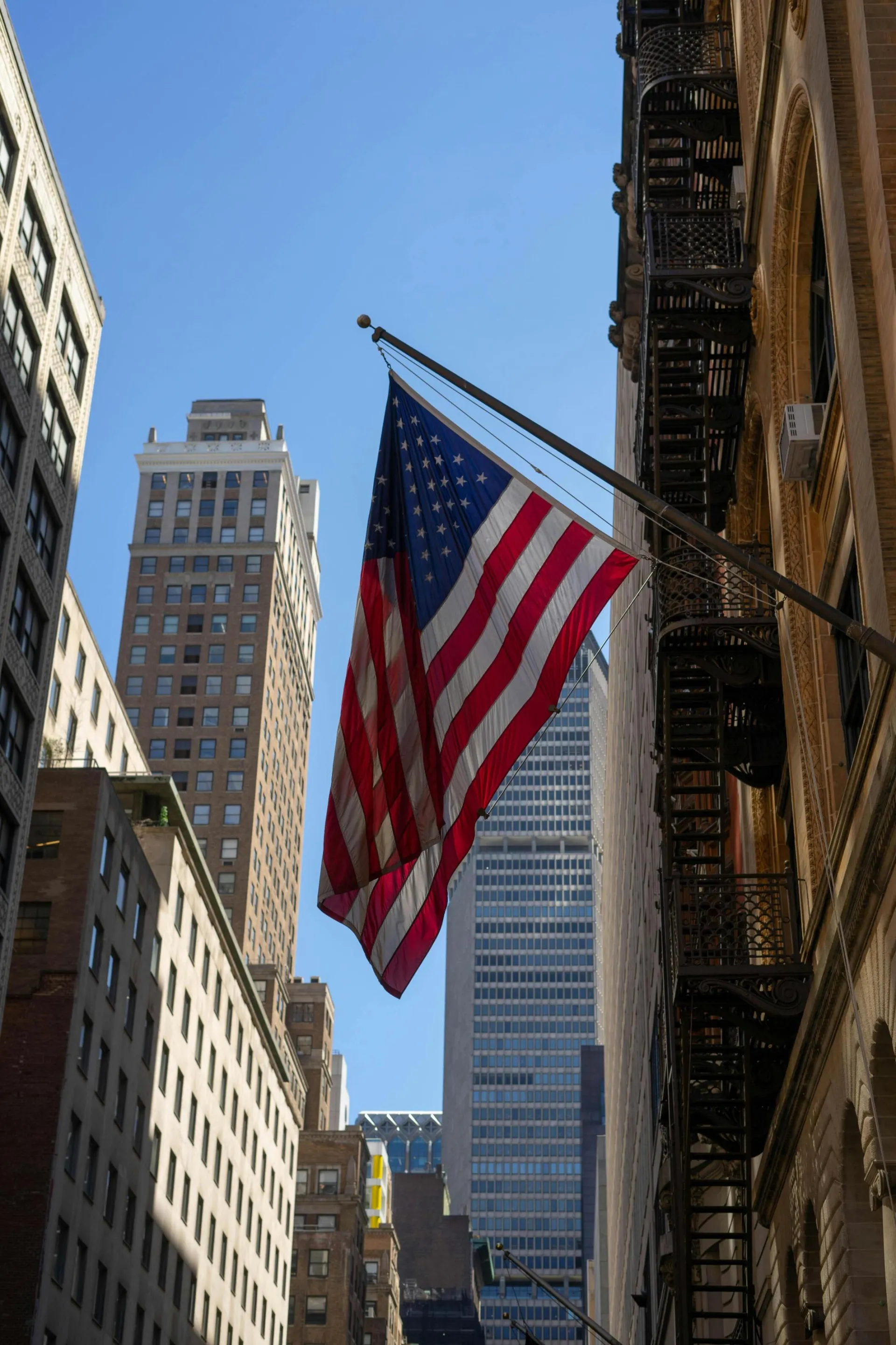 A low angle view of an American flag waving among New York skyscrapers.