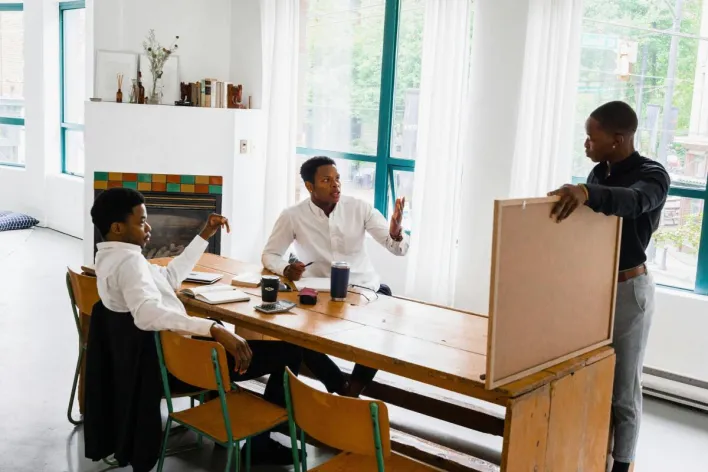 Three men discussing a project at a table in a bright office setting.