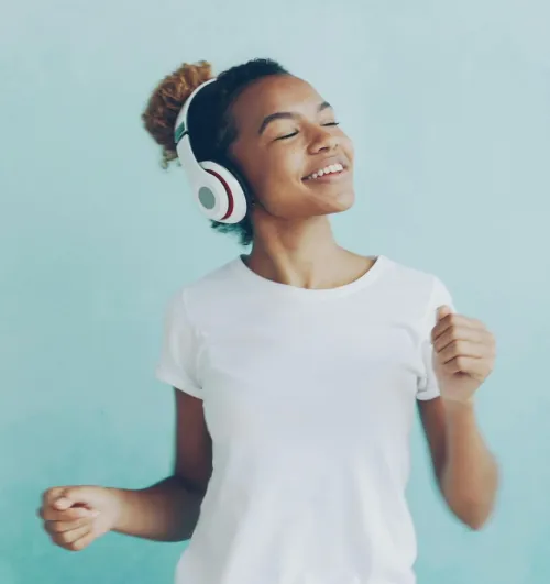 Smiling young woman listening to music with headphones against a blue background.