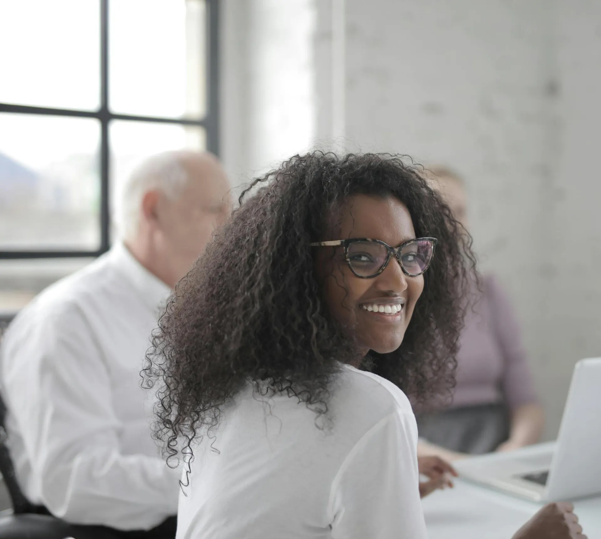 Positive ethnic woman with laptop smiling while sitting at table with coworkers and working together during business meeting in contemporary office