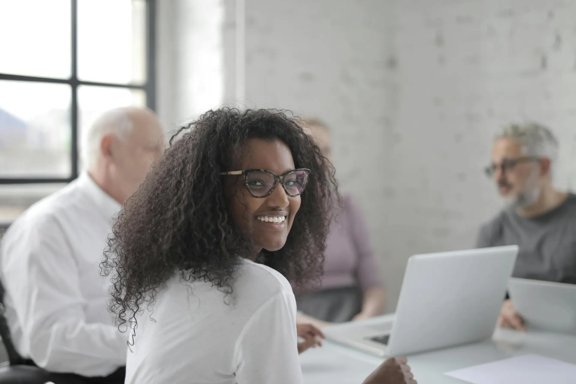 Positive ethnic woman with laptop smiling while sitting at table with coworkers and working together during business meeting in contemporary office